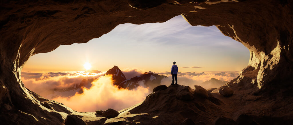 Adventurous Man Hiker standing in a cave with rocky mountains